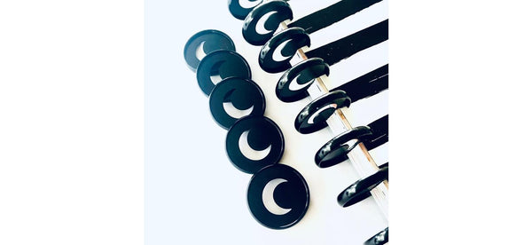 Close-up of black crescent moon cutout planner binding discs lined up diagonally beside a black disc-bound notebook spine