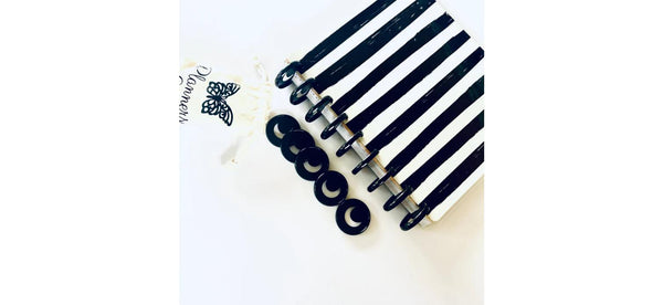 Five loose black crescent moon planner discs resting on a black and white striped disc-bound notebook, with a cream butterfly-print pouch in the corner