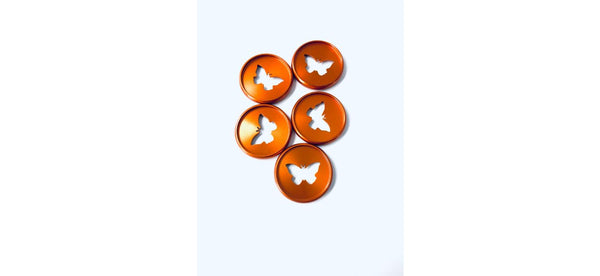 Five shiny bronze planner binding discs with butterfly-shaped cutouts arranged in a loose cluster on a white background
