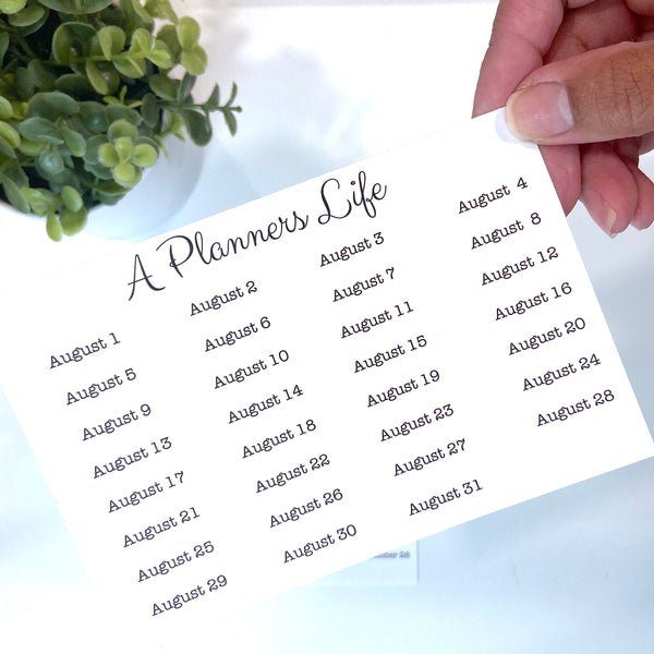 Hand holding a sheet of August date stickers next to a small potted plant