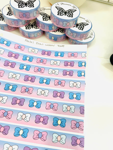 Washi tape rolls next to an unrolled sheet of pastel bow pattern washi tape