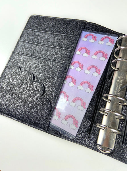 Partial rainbow and cloud vellum sticker sheet in a narrow pocket page inside an open black ring-bound planner
