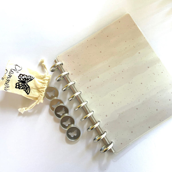 Silver 28mm planner discs stacked beside a small cream drawstring storage pouch with a butterfly logo, resting on a disc-bound notebook